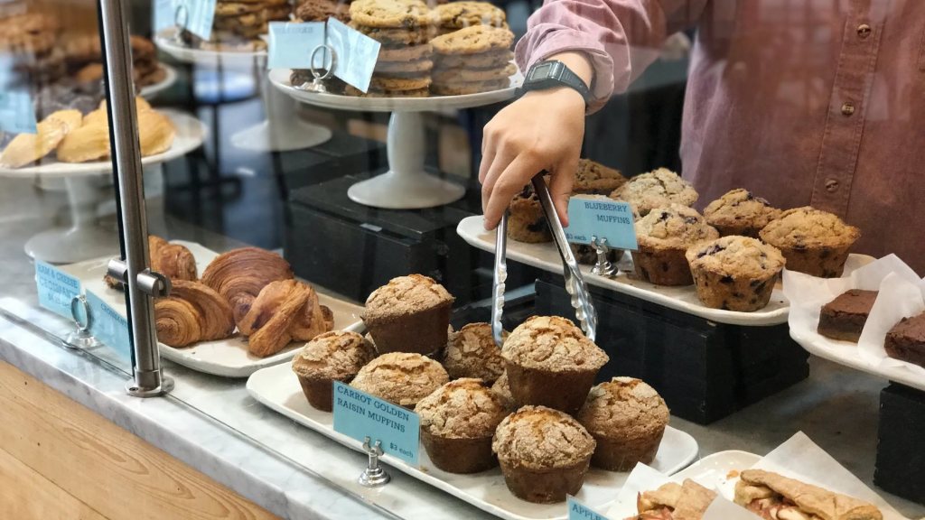 A hand with a large tong in a pastry display case at Dozen Bakery in Nashville