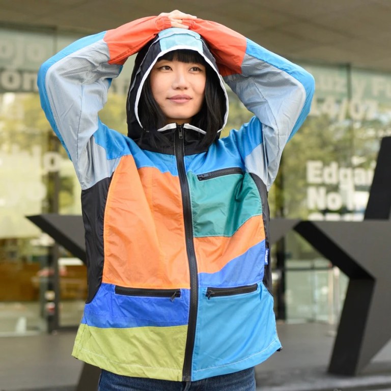 A woman wears a jckets made from upcycled parachute fabric with colorful panels