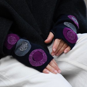A pair of black fingerless gloves with several two-tone fabric circle appliqués worn on a woman's hands