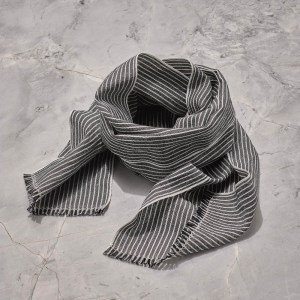A handwoven scarf with black and white stripes in Long staple Egyptian cotton woven with finely spun European line is folded in a circle on a counter top
