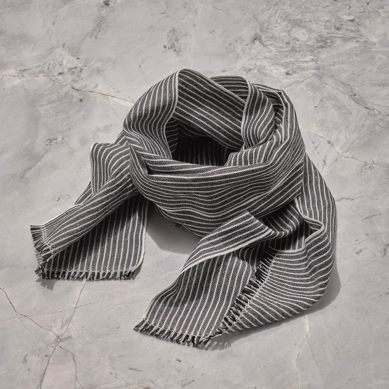 A handwoven scarf with black and white stripes in Long staple Egyptian cotton woven with finely spun European line is folded in a circle on a counter top