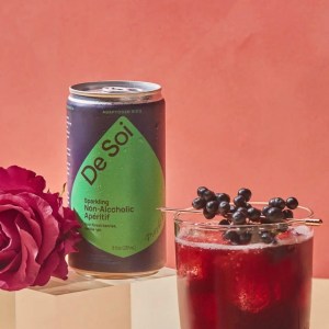 A can of Se Soi on a table top with a rose and a glass of the beverage with berries in it
