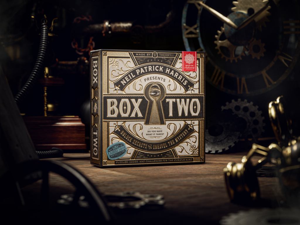 brown and gold game box on a wood floor surrounded by clocks and gears