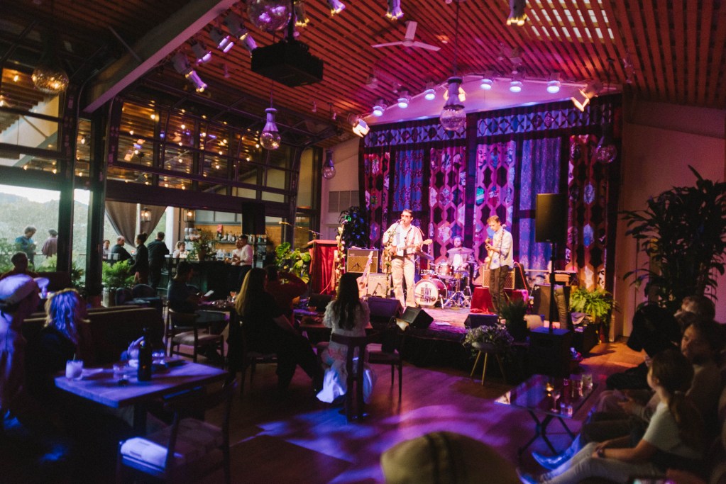 intimate performance venue with three musicians on stage under purple lighting