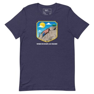 A blue t-shirt featuring an illustration of a mountain with an upside down flag and the mottow "When in Doubt, Go Higher"