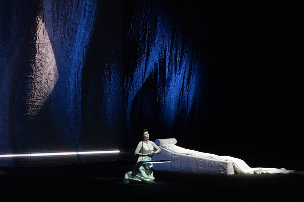 A woman performs on a stage with a hanging chair, a lounge chair, with blue curtains