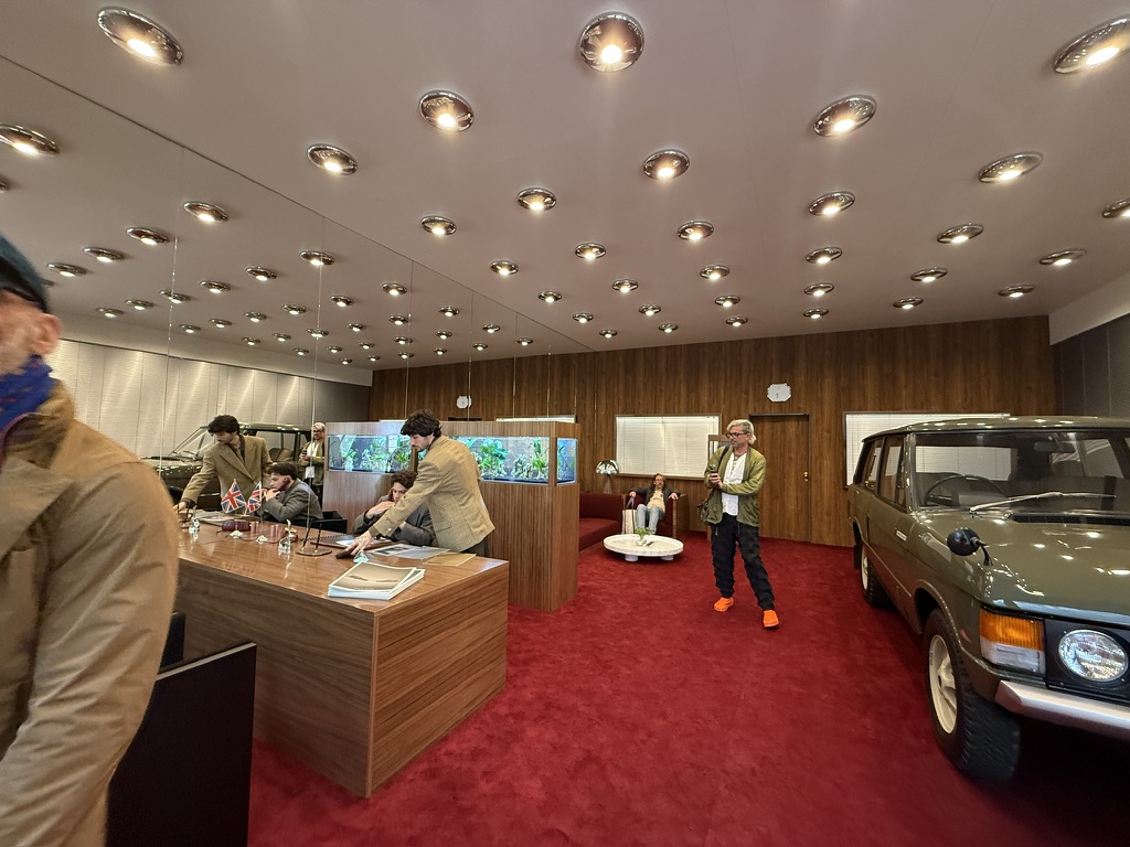 A set with a 1970s London vibe—a wood desk, a fish tank, chrome lights, and a 1970 Range Rover in original green