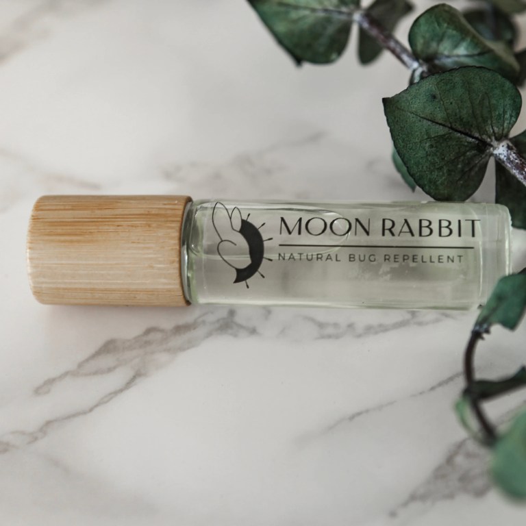 A glass cyclinder of Moon Rabbit's natural bug repellent on a counter with a branch
