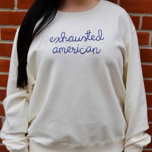 A model wears a white sweatshirt with the words "exhausted american" embroidered on it
