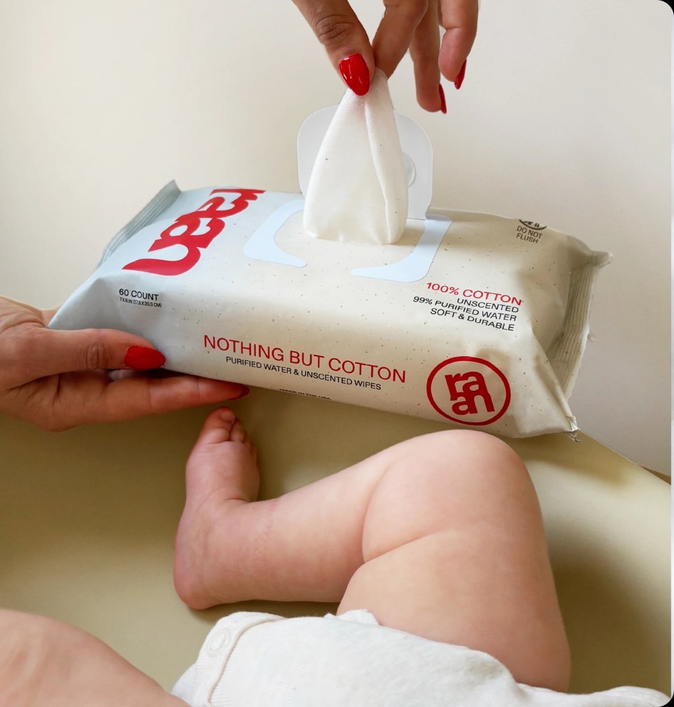 A woman's hand pulls a Raan cotton wipe from a package next to a baby's leg