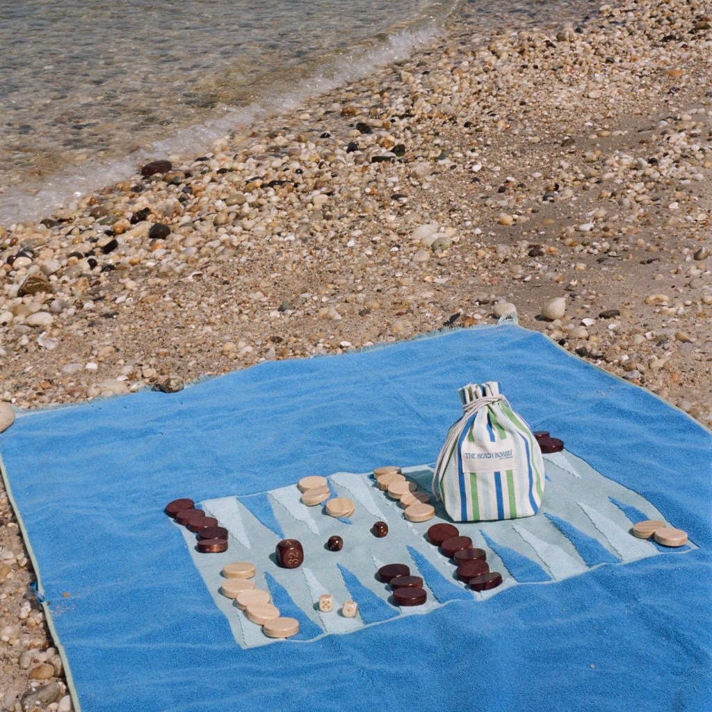 A G. McGee beach towel with a backgammon board woven into it, and a bag full of backgammon game pieces