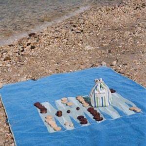 A G. McGee beach towel with a backgammon board woven into it, and a bag full of backgammon game pieces