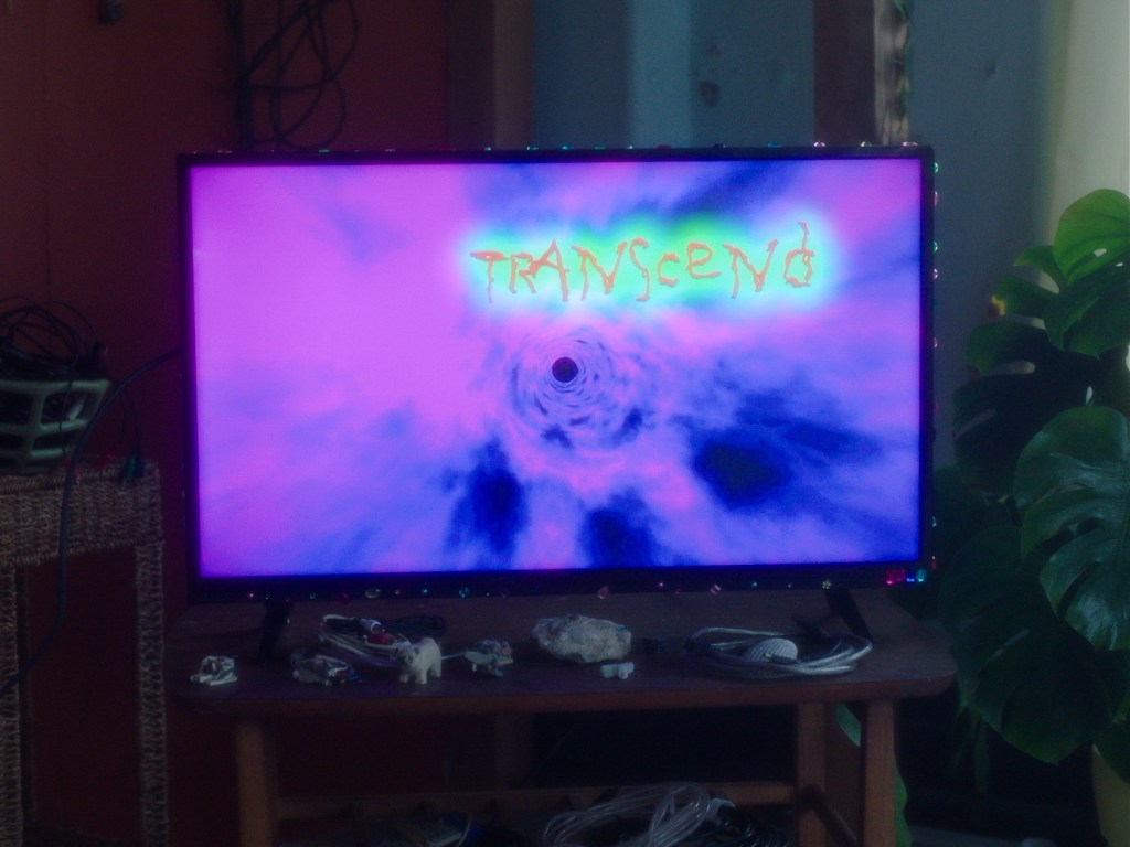 A tv screen with a pink and blue blurry pattern on it says Transcend in orange and aqua glowy text