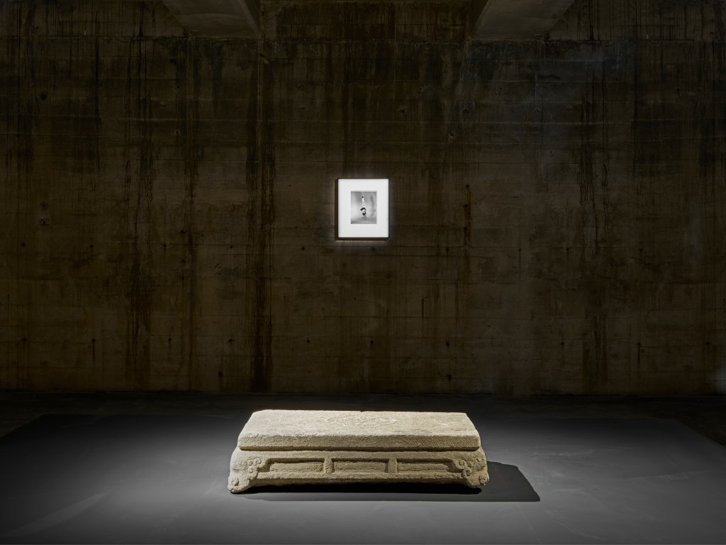 A photograph hanging on a dark gallery wall above an antique stone platform.
