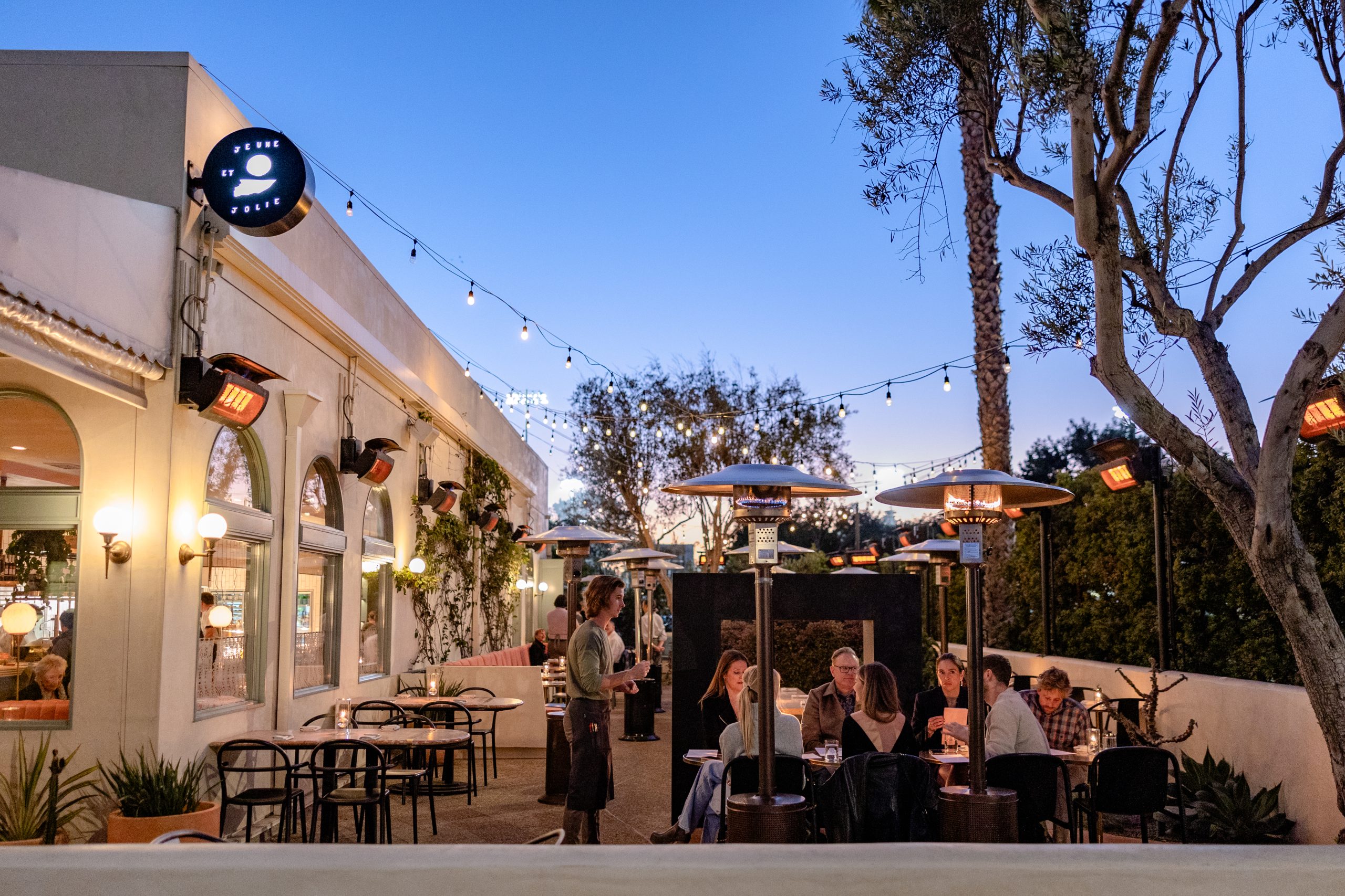 A restaurant patio with people dining outside and a waitress serving a table