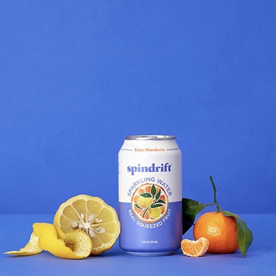 A can of SPindrift's Yuzu Mandarin sparkling water alongside a peeled yuzu and a mandarin
