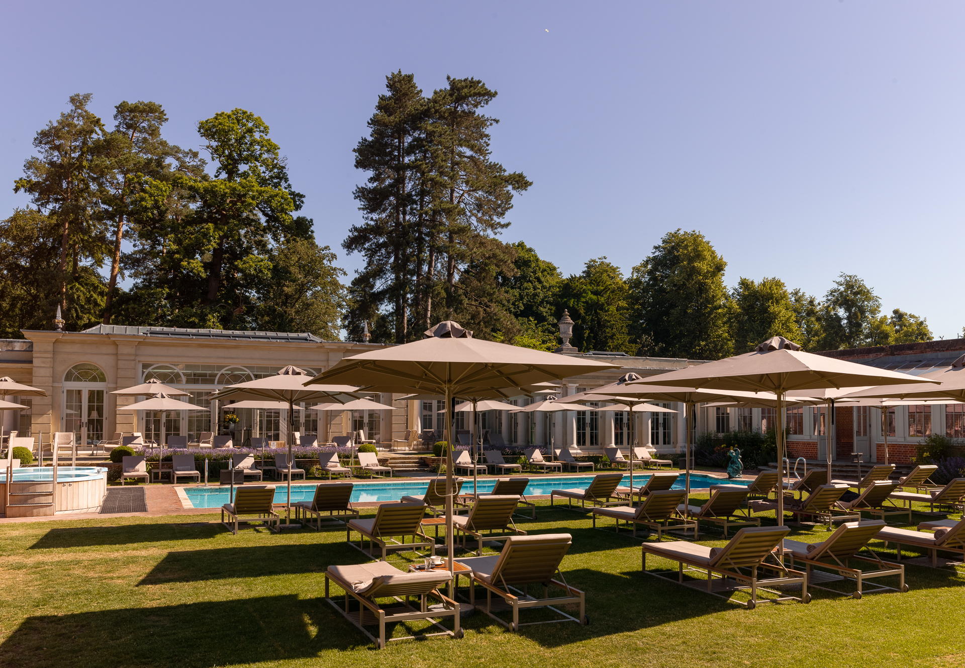 A pool surrounded by grass, lounge chairs and umbrellas.