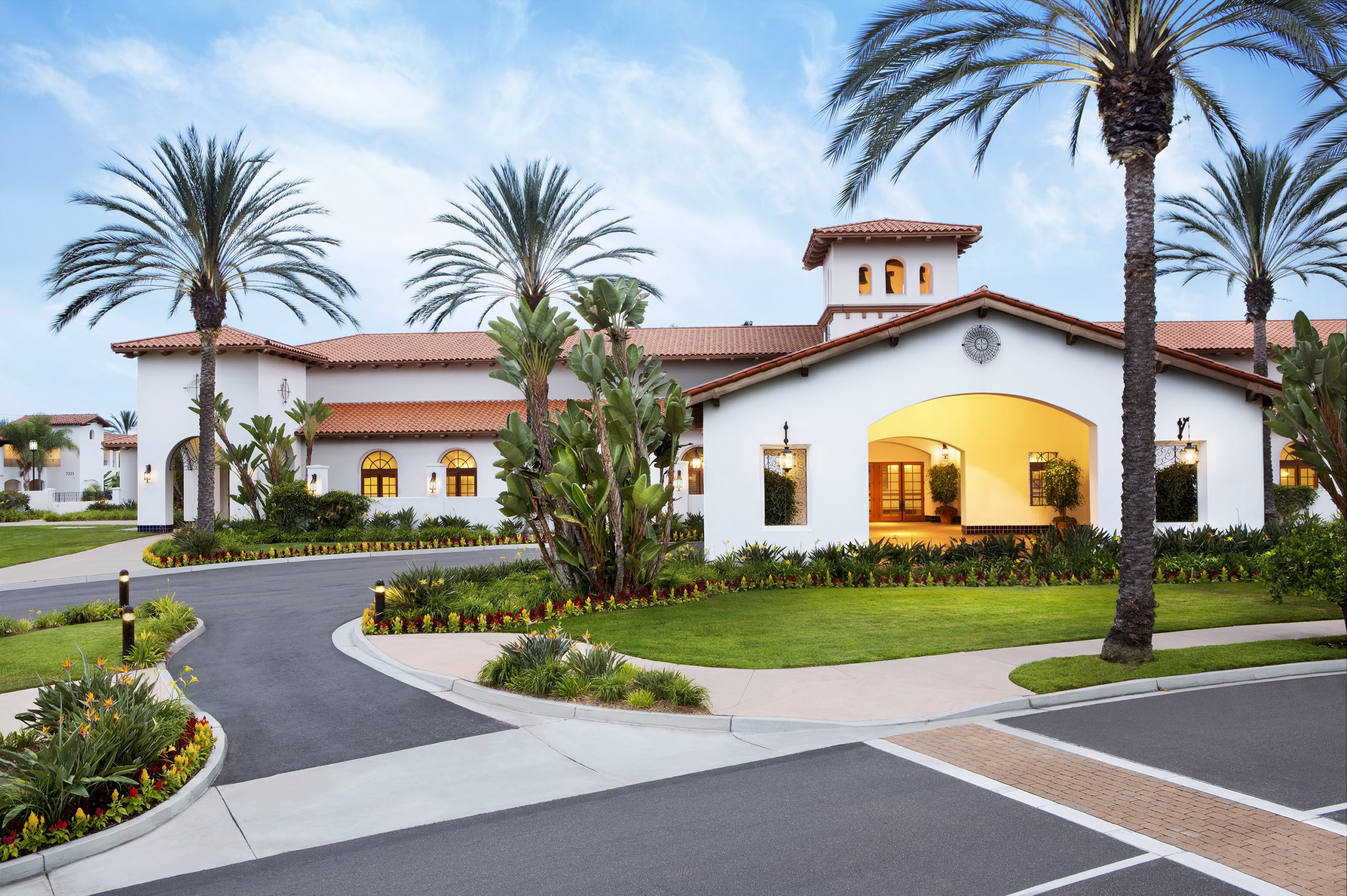 an exterior view of a white spa building with grass, palm trees and a driveway
