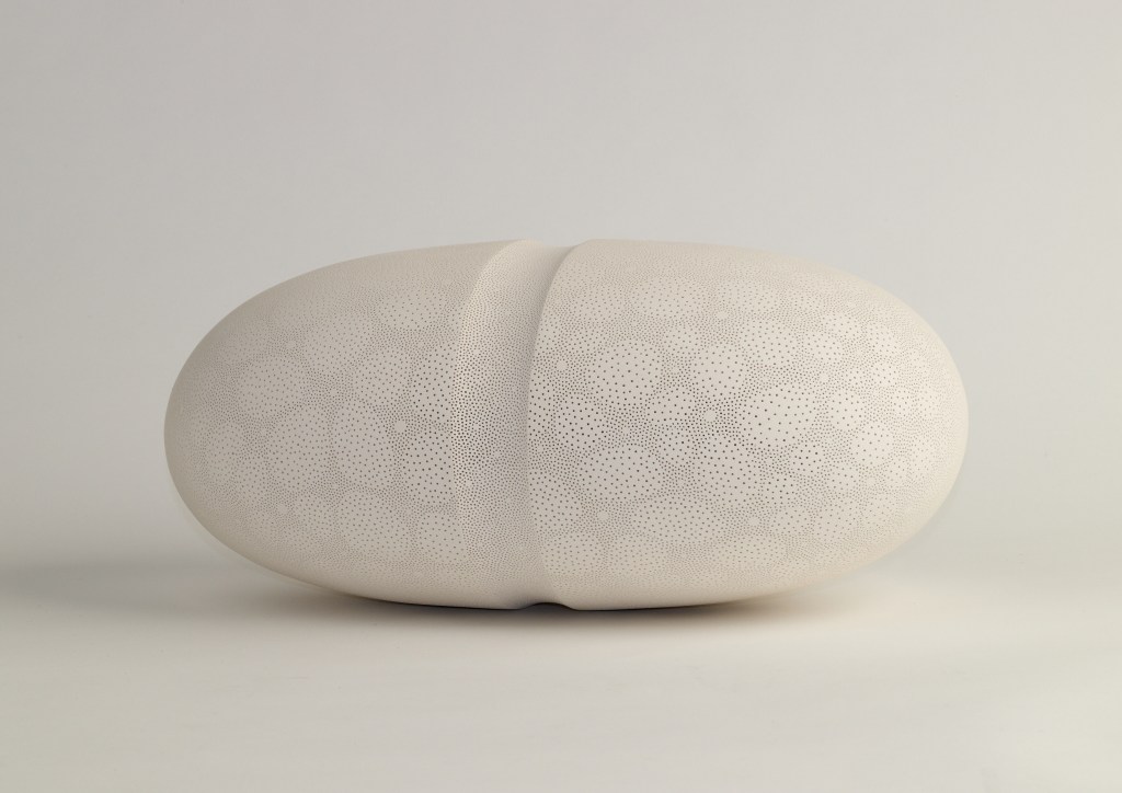 An oblong white sculpture with tiny speckles on a white surface.