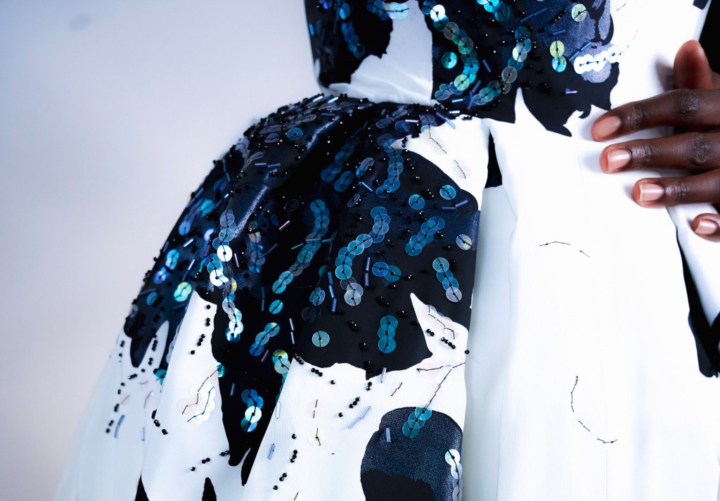 A closeup of a white gown with a navy blue floral print and blue sequins with a woman's hand at the waist.