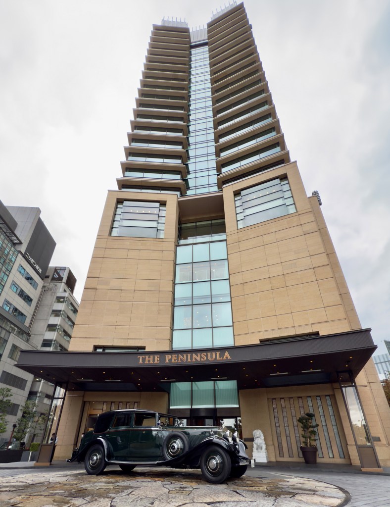 Tokyo's The Peninsula Hotel shot from the front looking up at the building with a vintage Rolls-Royce in front.