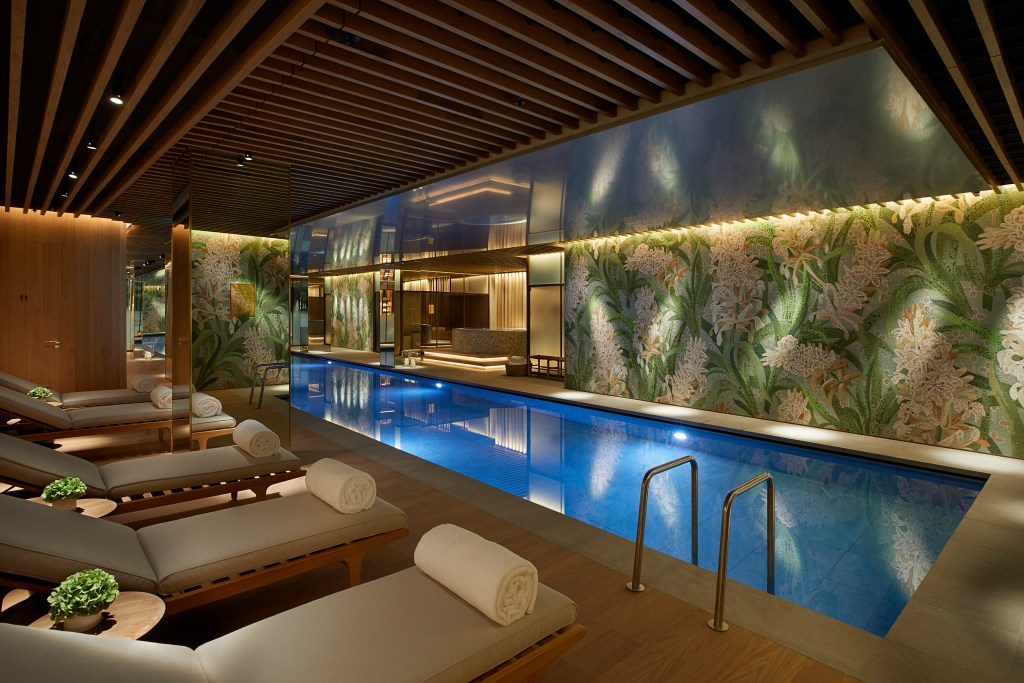 An indoor pool surrounded by wood, mosaic tiled walls, and mirrors. 