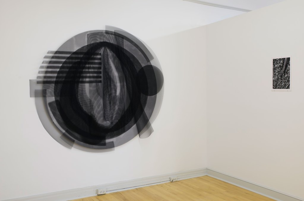 Two pieces of black and white abstract art hanging on a white walled gallery corner.