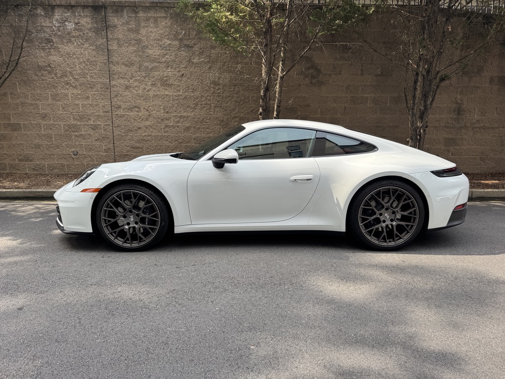 A white Porsche 911 Carrera parked next to a wall.