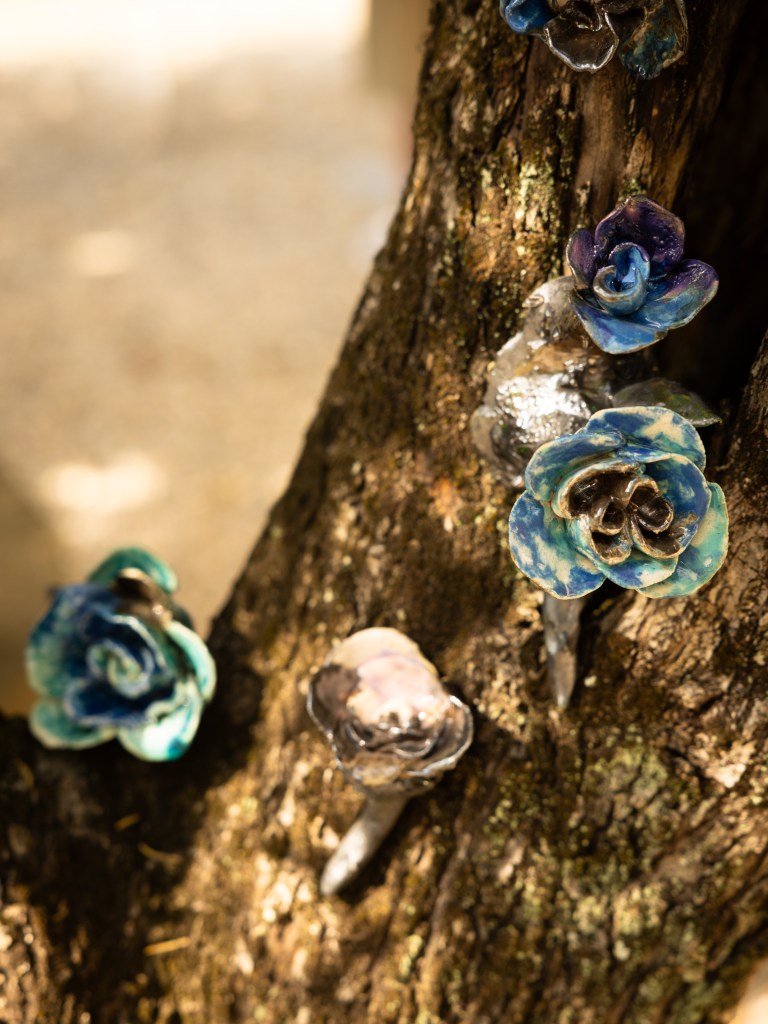 A detail of Ilaria d'Atri's ceramic flower sculptures on a tree branch.