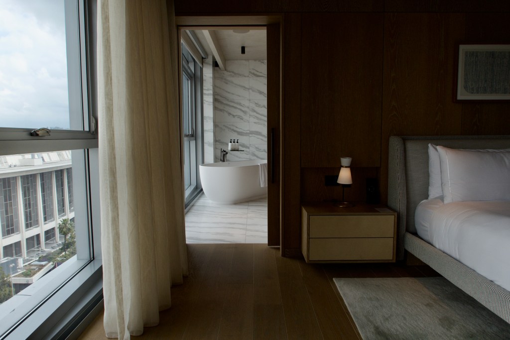 A suite at The Conrad Hotel with a soaking tub by a window.