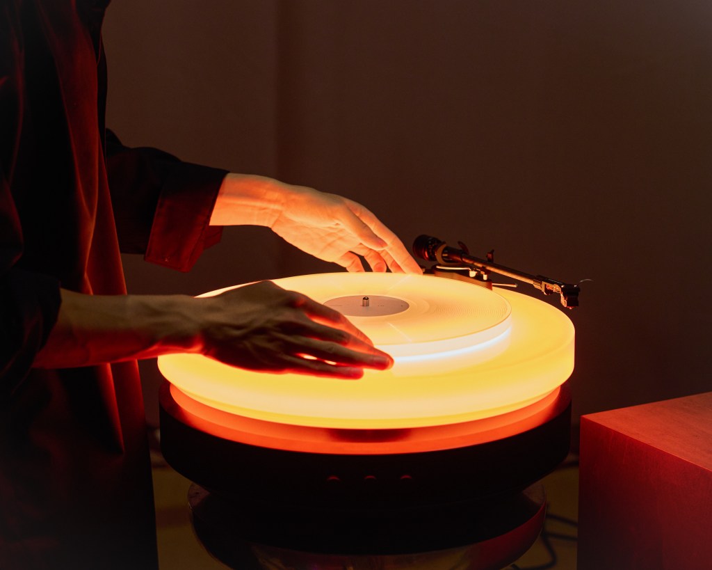 A DJ playing a recond on a glowing orange turntable.