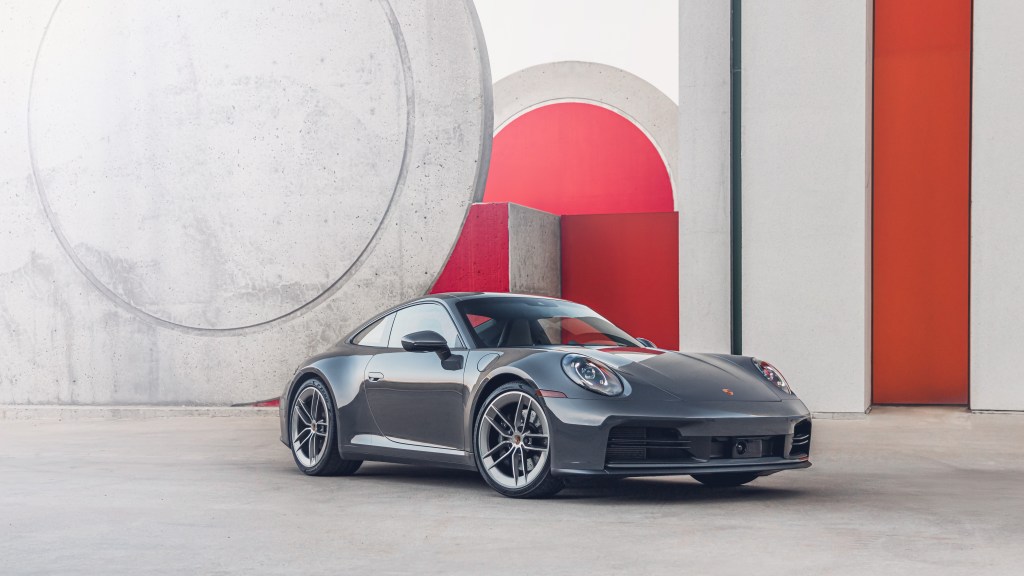 A slate grey Porsche 911 Carrera parked in front of a red and concrete wall.