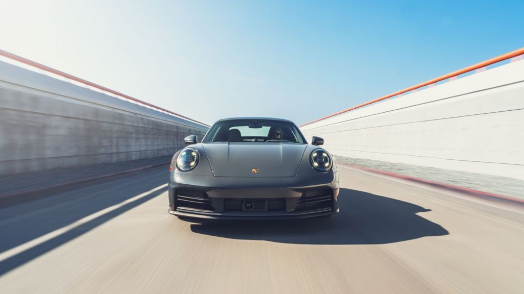 A slate grey Porsche 911 Carrera driving on a road.