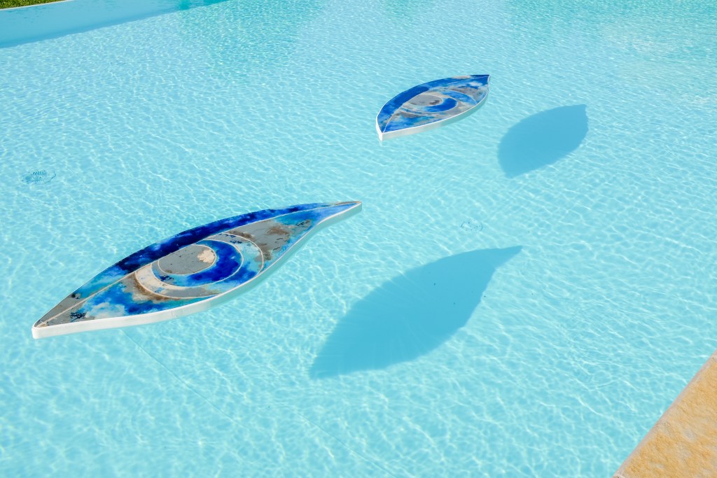 Two eye sculptures by Sara Ricciardi float in a swimming pool