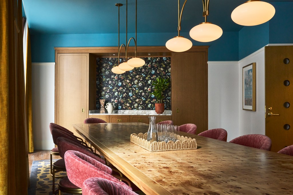 A long table at Fidelity Hotel with brass light fixtures and floral wallpaper.