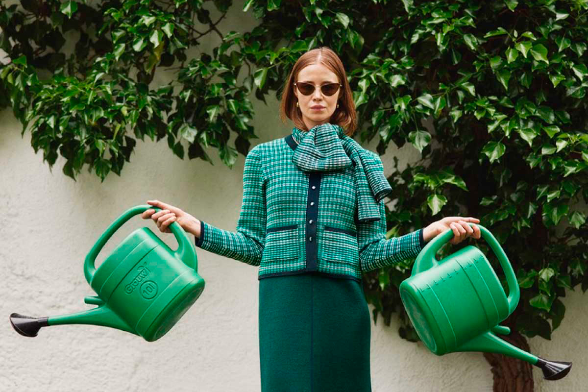 A model wearing a green Oleana outfit while holding two green watering cans.