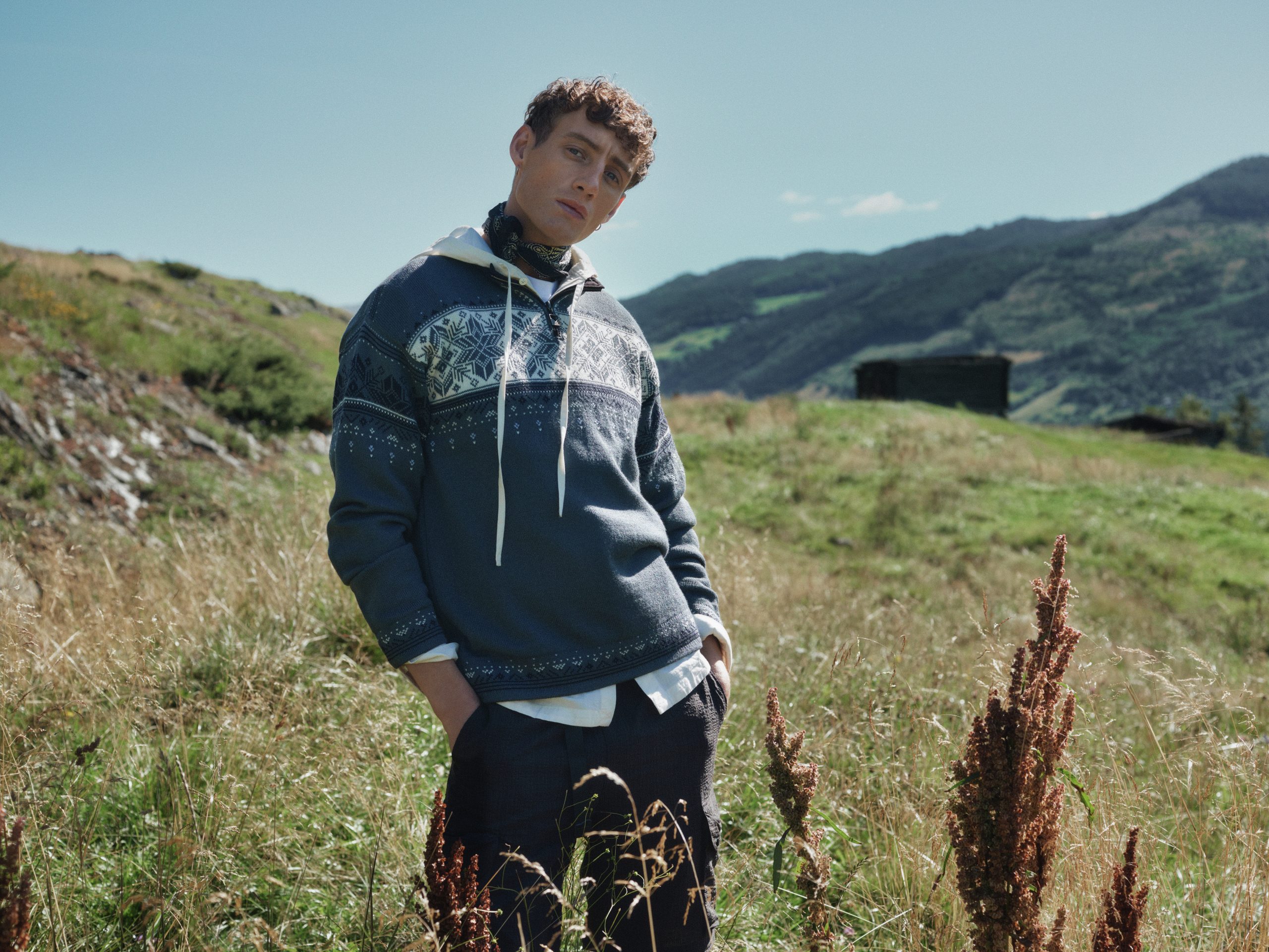A male model standing on a grassy hillside wearing a Dale of Norway sweater.