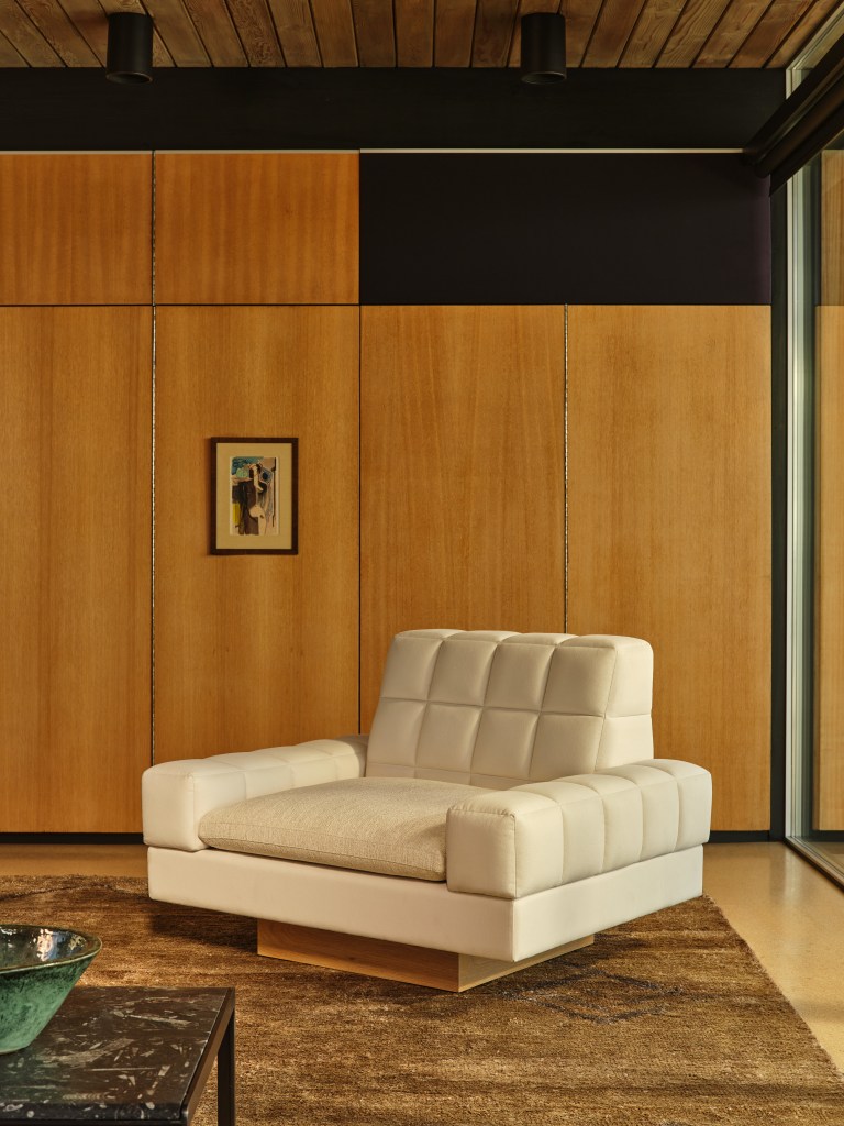 A white cubic chair on a square wood base against a wooden wall.