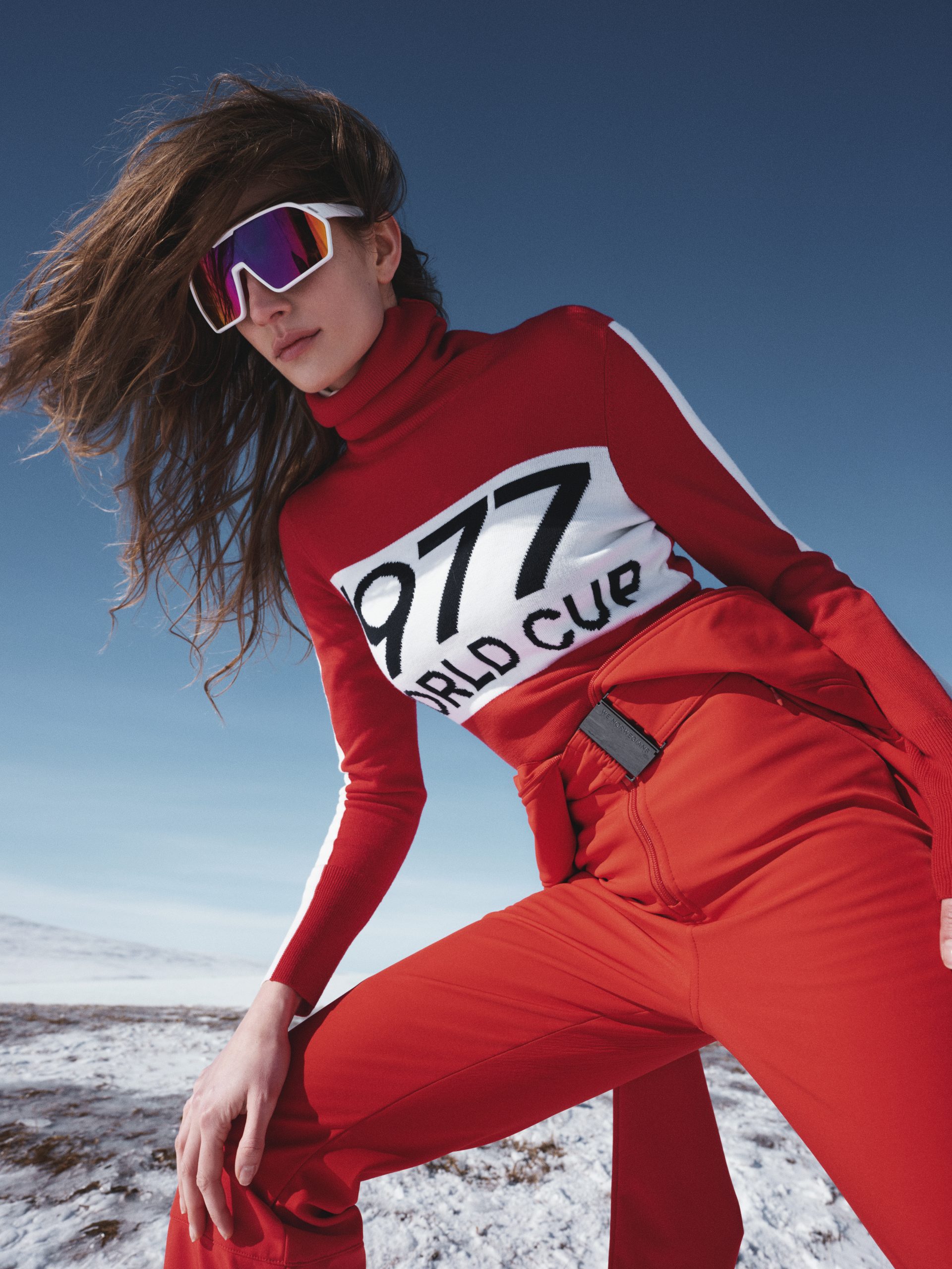 A model outside on a mountain wears a red ski outfit by We Norwegians.