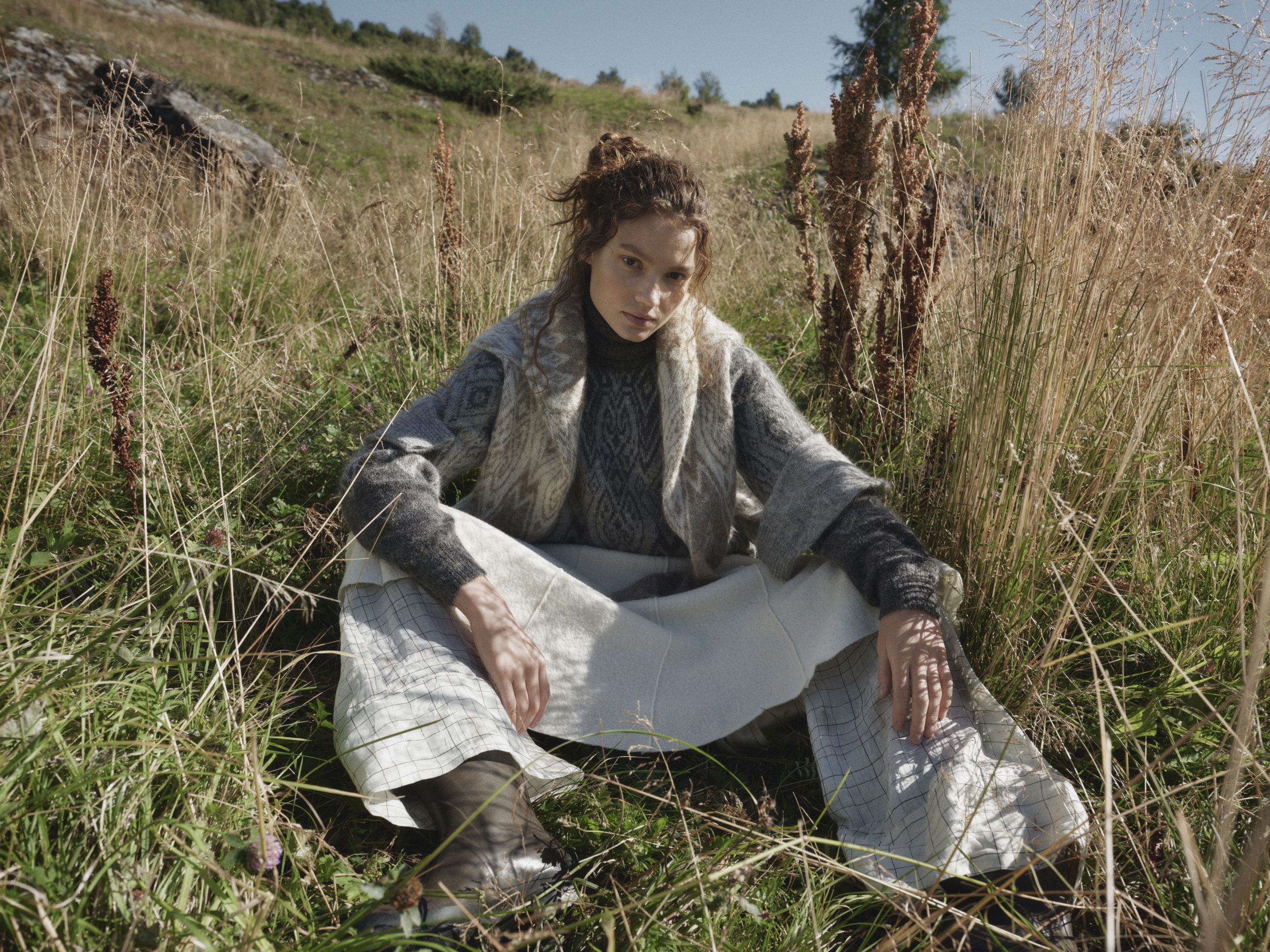 A model sitting in the grass wearing a Dale of Norway sweater.