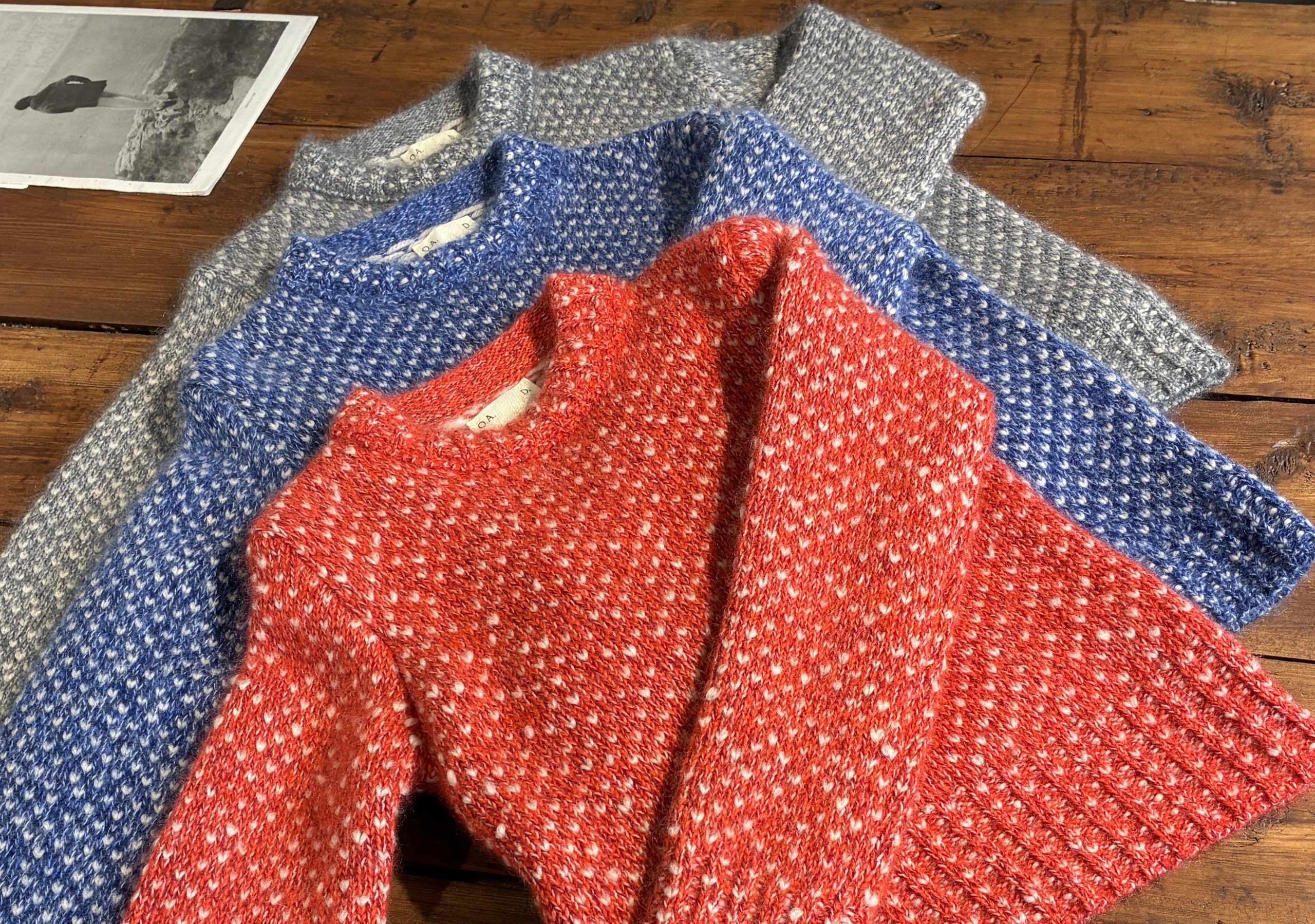 A trio of colorful O.A.D. sweaters layered on top of a wood tabletop.