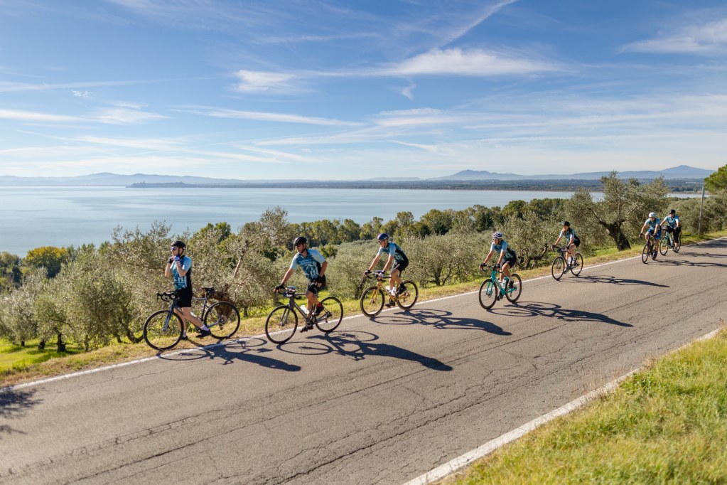 A group of cyclists riding in a line on a Tuscan road.