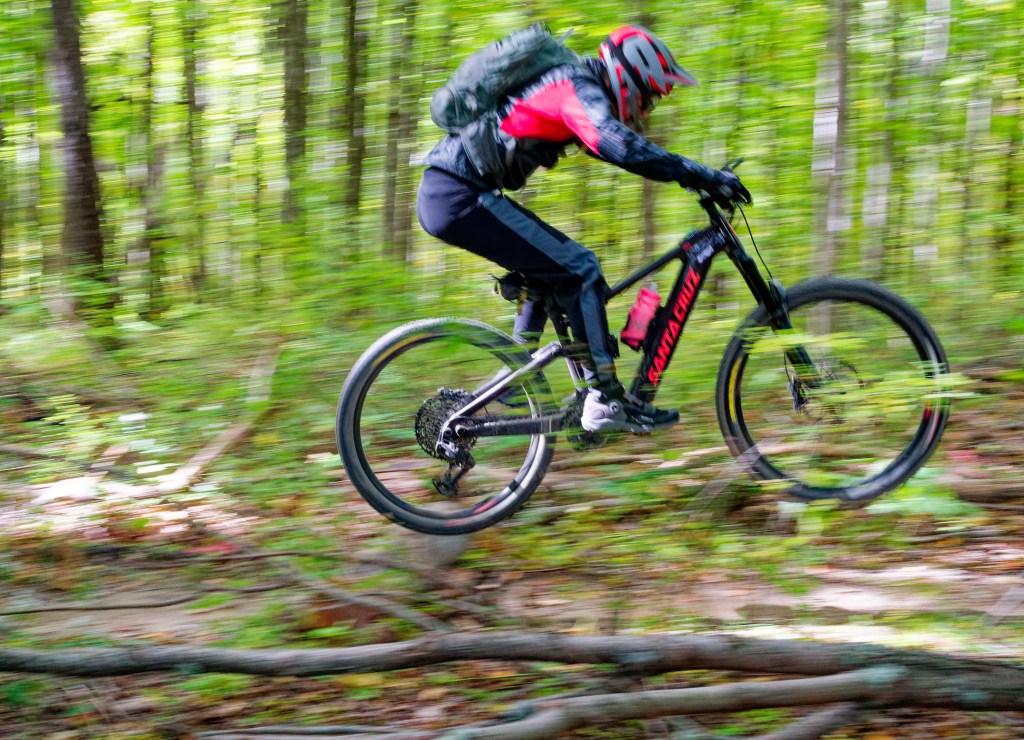 A mountain biker riding the Santa Cruz Vala Alu 70 bike through the woods.
