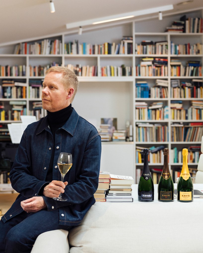 Composer Max Richter sitting on a sofa ledge with three bottles of Krug 2008 vintages.