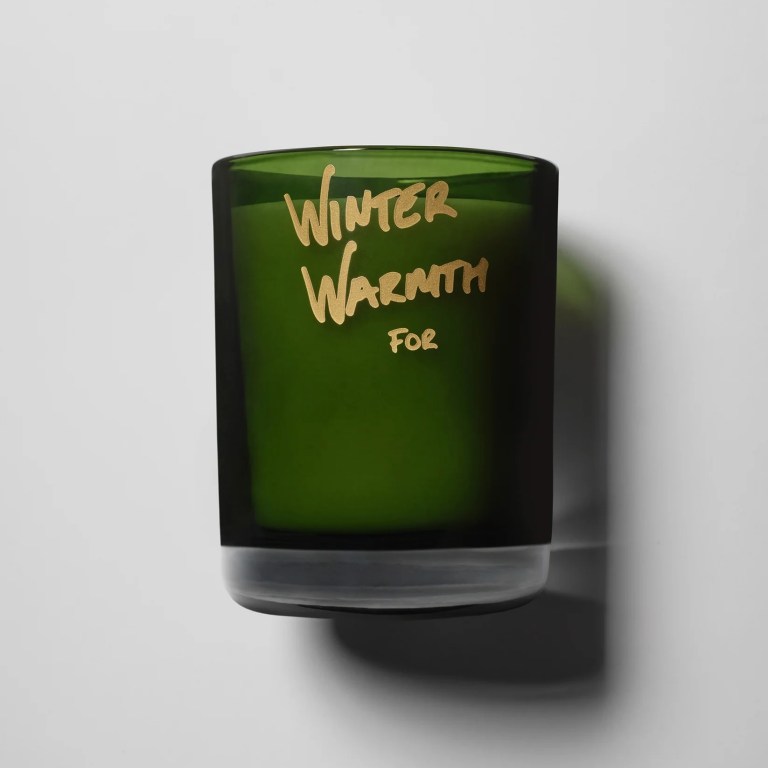 A candle in a green glass container, with gold writing that says Winter Warmth for