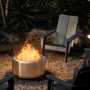 Solo Stove's Smokeless Fire Pit is shown on the ground outside, surrounded by chairs, with flames and no smoke