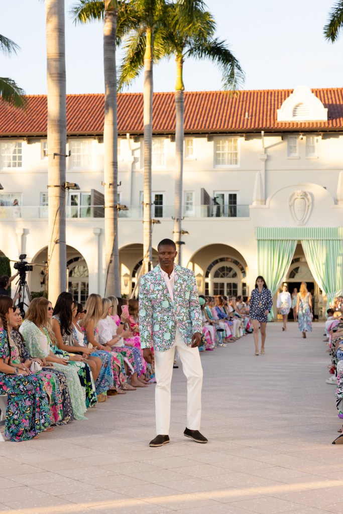 A male model at the Lilly Pulitzer Spring 2026 show wearing a light blue and pink printed blazer with white trousers.