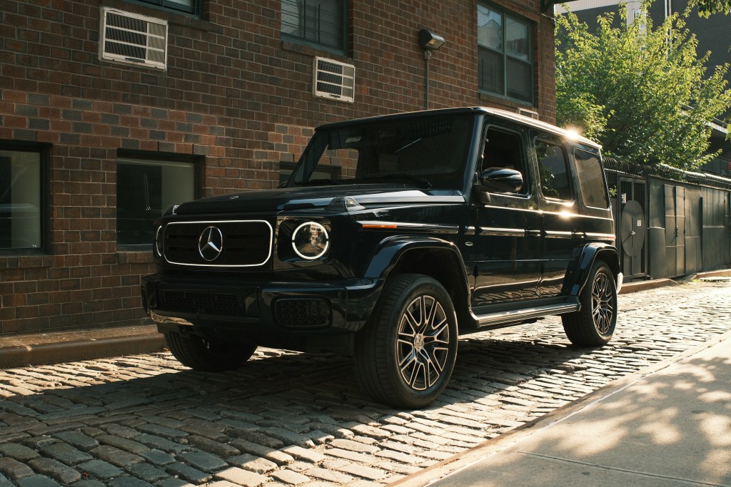 A Mercedes-Benz G-580 parked in front of a brick building on a cobblestone street.
