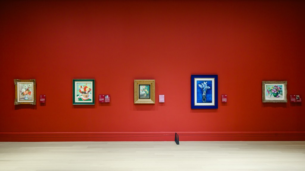 A red wall in Deji Art Museum with five framed flower paintings.