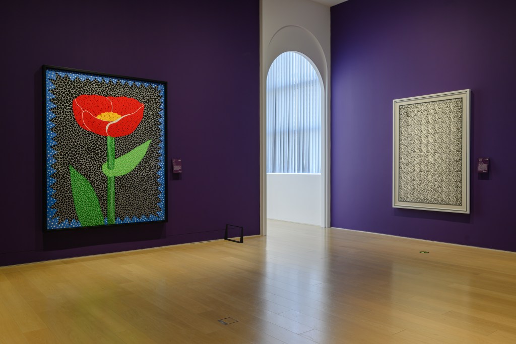 A purple walled gallery with two large paintings flanking an arched doorway.